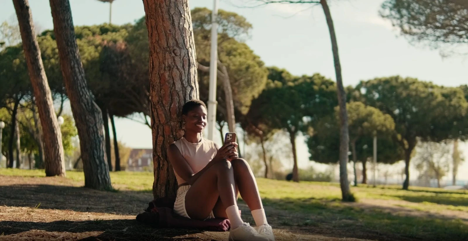 A student sitting under a tree, phone in hand.