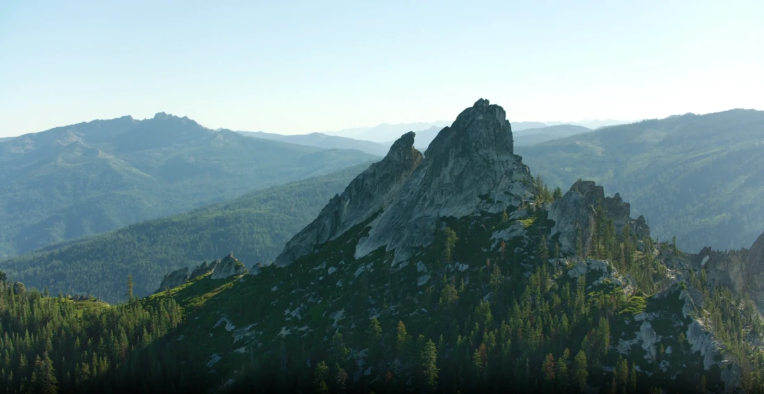 A rock tower above forested slopes in a national park at dusk.