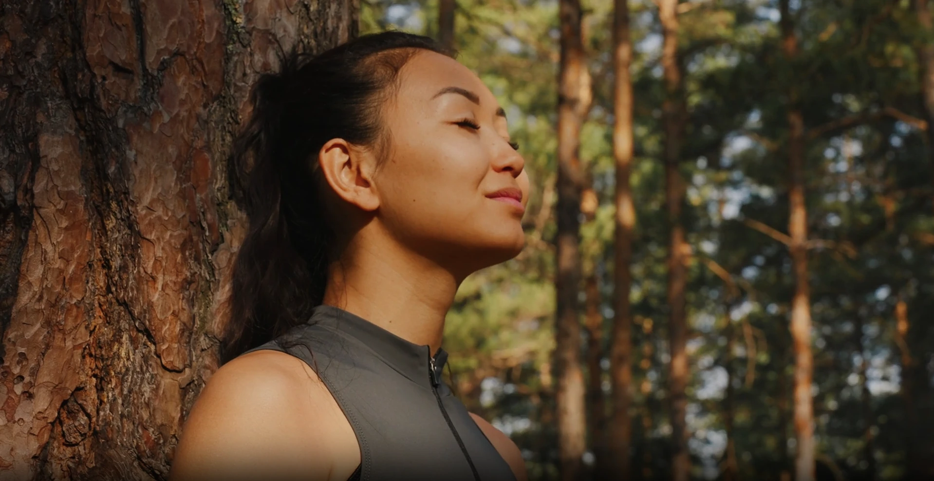 A student resting against a pine, eyes closed.